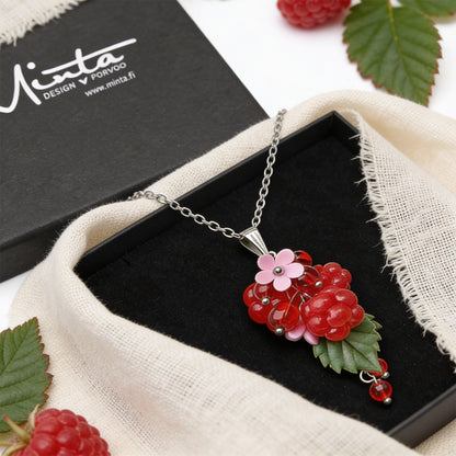 Raspberry Garden Necklace presented in a gift box, featuring hand-shaped berries and leaves, surrounded by natural linen fabric, fresh raspberries, green leaves, and delicate white flowers in soft natural light. Handmade in Finland by byMinta.