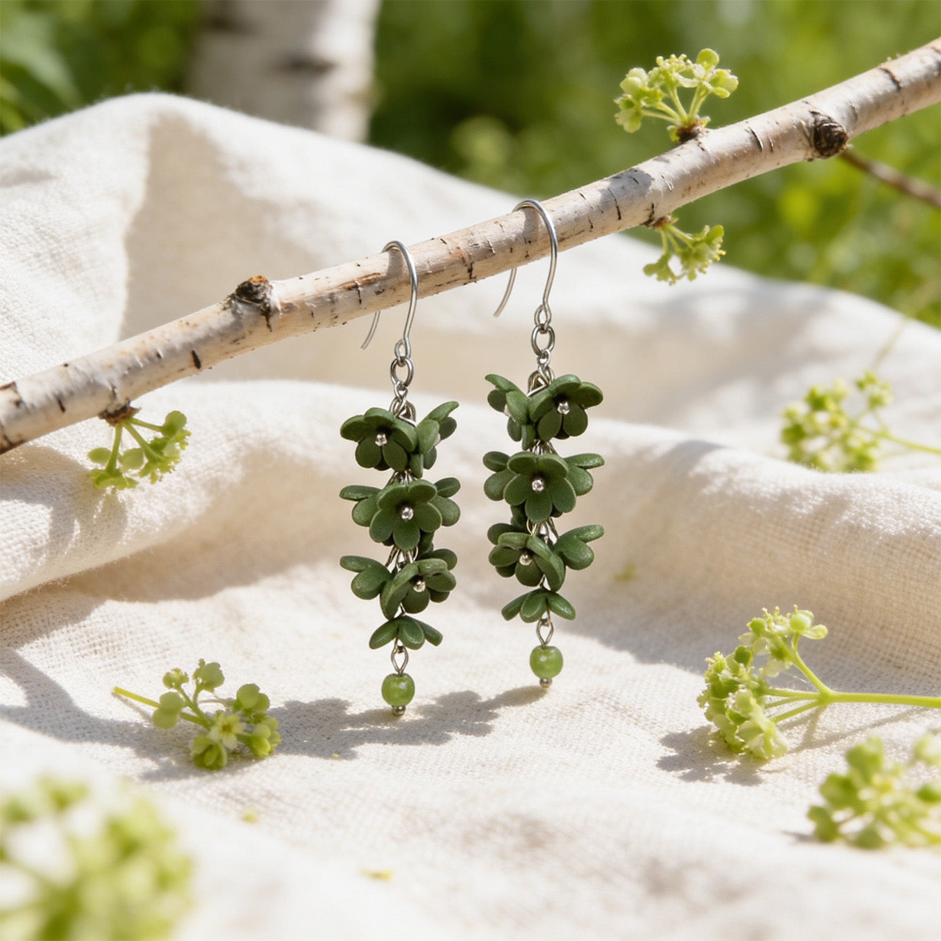 Shadow Vine Green Earrings displayed on a birch branch in bright natural daylight. Handmade in Finland by byMinta.
