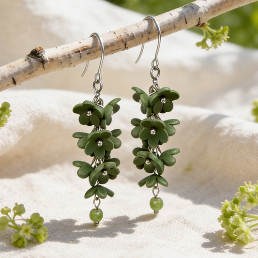 Shadow Vine Green Earrings displayed on a birch branch in bright natural daylight. Handmade in Finland by byMinta.
