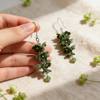 Shadow Vine Green Earrings photographed in soft natural light, with one earring gently held by hand for scale. Handmade in Finland by byMinta.