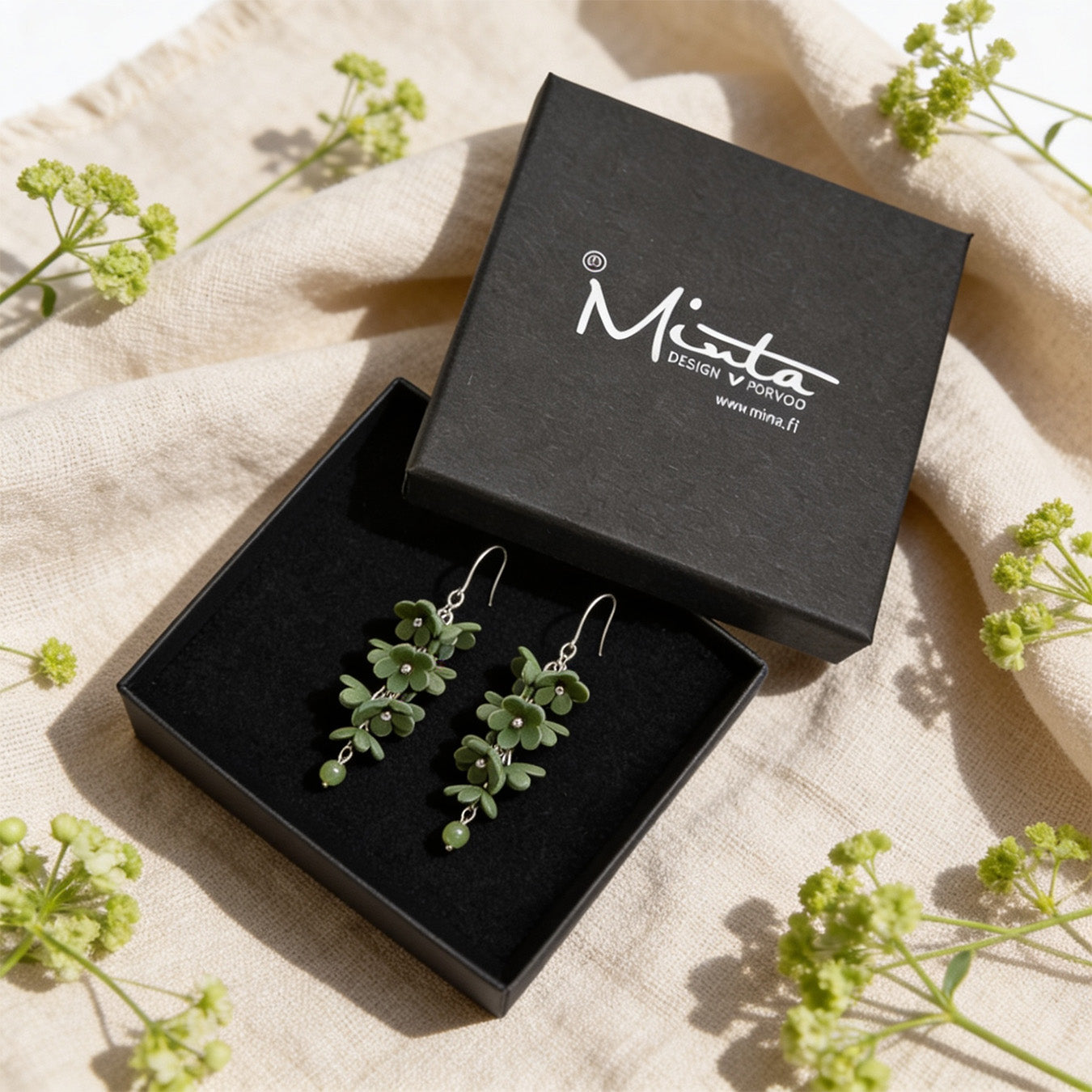 Shadow Vine Green Earrings presented in a gift box, surrounded by natural linen fabric and delicate green flowers. Handmade in Finland by byMinta.
