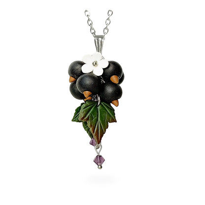Handmade berry necklace featuring sculpted blackcurrants, detailed green leaves, a small white flower and purple crystal accents. Botanical statement jewelry on a fine chain against a clean white background, handcrafted in Finland.