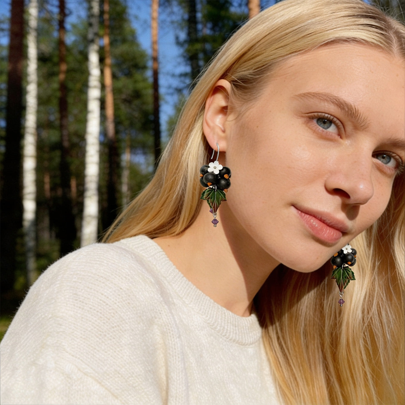 Blonde woman wearing Shadow Currant Earrings in a sunlit Nordic forest. Handmade earrings inspired by the mysterious beauty of dark forest berries.