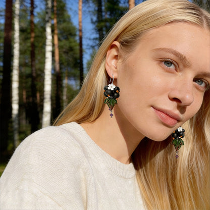Blonde woman wearing Shadow Currant Earrings in a sunlit Nordic forest. Handmade earrings inspired by the mysterious beauty of dark forest berries.