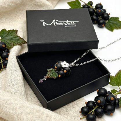 Shadow Currant Necklace presented in a gift box, surrounded by natural linen fabric, black currants, and black currant leaves in soft natural light. Handmade necklace with hand-shaped berries and leaves, handmade in Finland by byMinta.