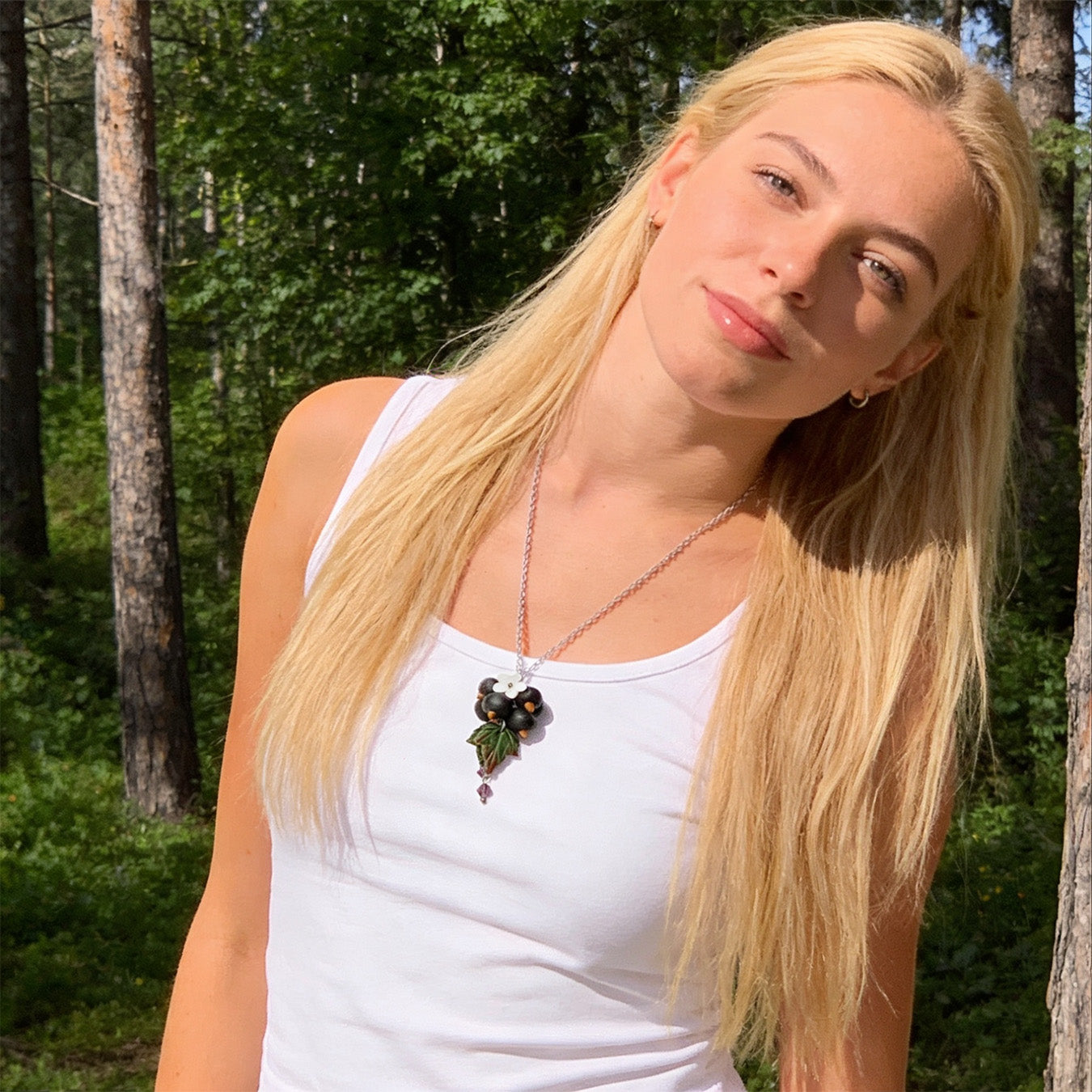 Blonde woman wearing the Shadow Currant Necklace in a sunlit Nordic forest. Handmade necklace with hand-shaped black currants and leaves, photographed in natural summer light. Handmade in Finland by byMinta.