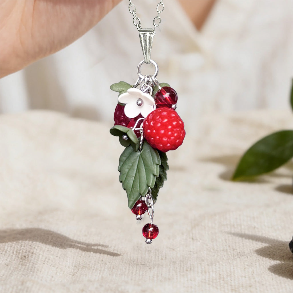 Handmade Wild Raspberry necklace with polymer clay raspberry, white flower, green leaves and red glass details. Nordic berry inspired jewelry handcrafted in Finland by byMinta.
