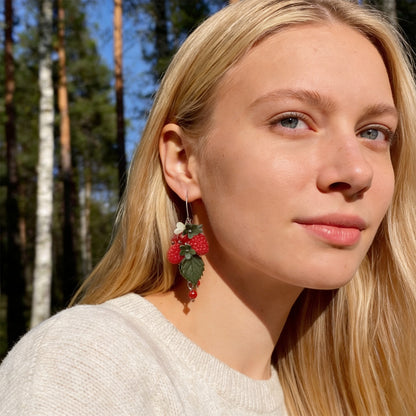 Blonde woman wearing Wild Raspberry Earrings in a sunlit Nordic forest. Handmade earrings inspired by the bright red glow of ripe wild raspberries.