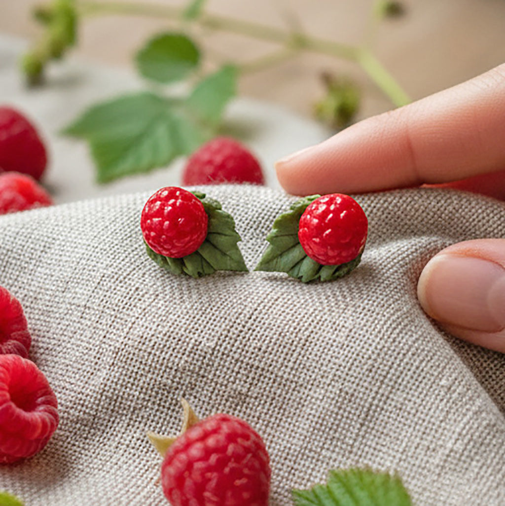 Handmade Wild Raspberry stud earrings with polymer clay berries on natural linen, surrounded by fresh raspberries and leaves. Nordic nature inspired jewelry handcrafted in Finland by byMinta.