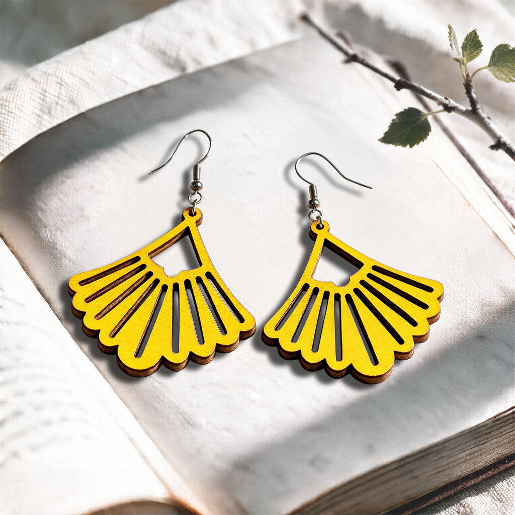 Yellow Fan plywood earrings made in Finland, photographed on a vintage book in natural sunlight