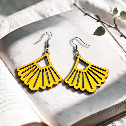 Yellow Fan plywood earrings made in Finland, photographed on a vintage book in natural sunlight