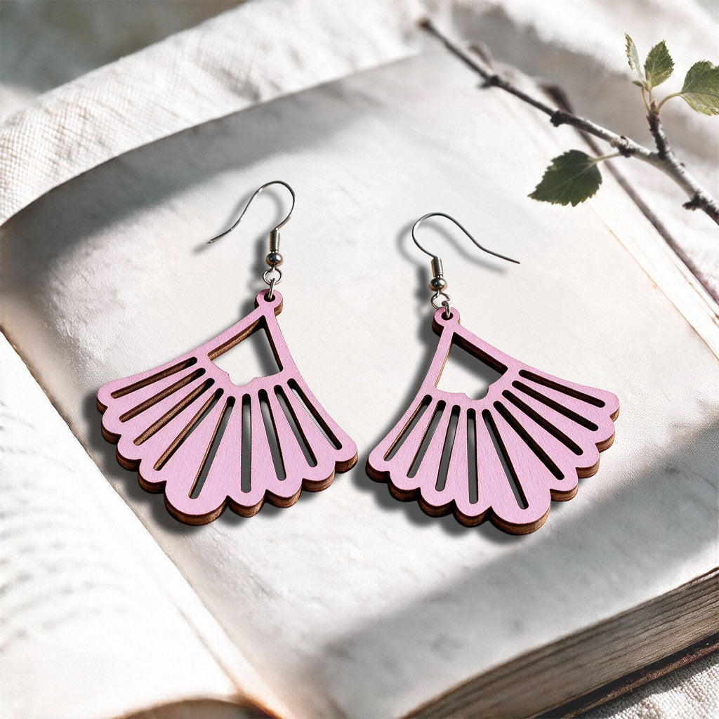 Mauve Fan plywood earrings made in Finland, photographed on a vintage book in natural sunlight