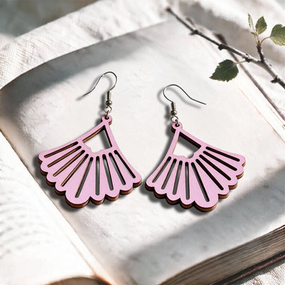 Mauve Fan plywood earrings made in Finland, photographed on a vintage book in natural sunlight