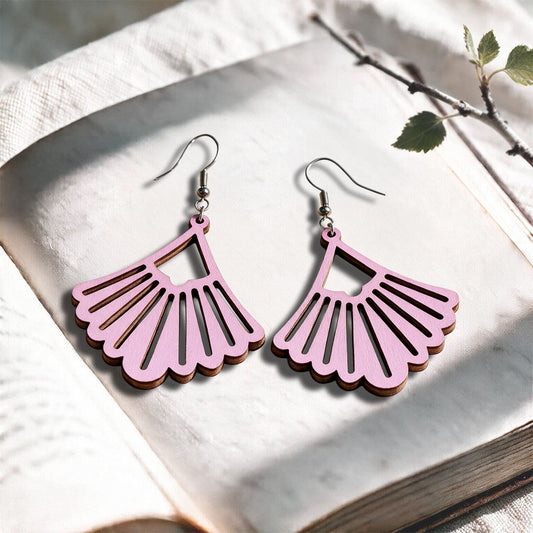 Mauve Fan plywood earrings made in Finland, photographed on a vintage book in natural sunlight