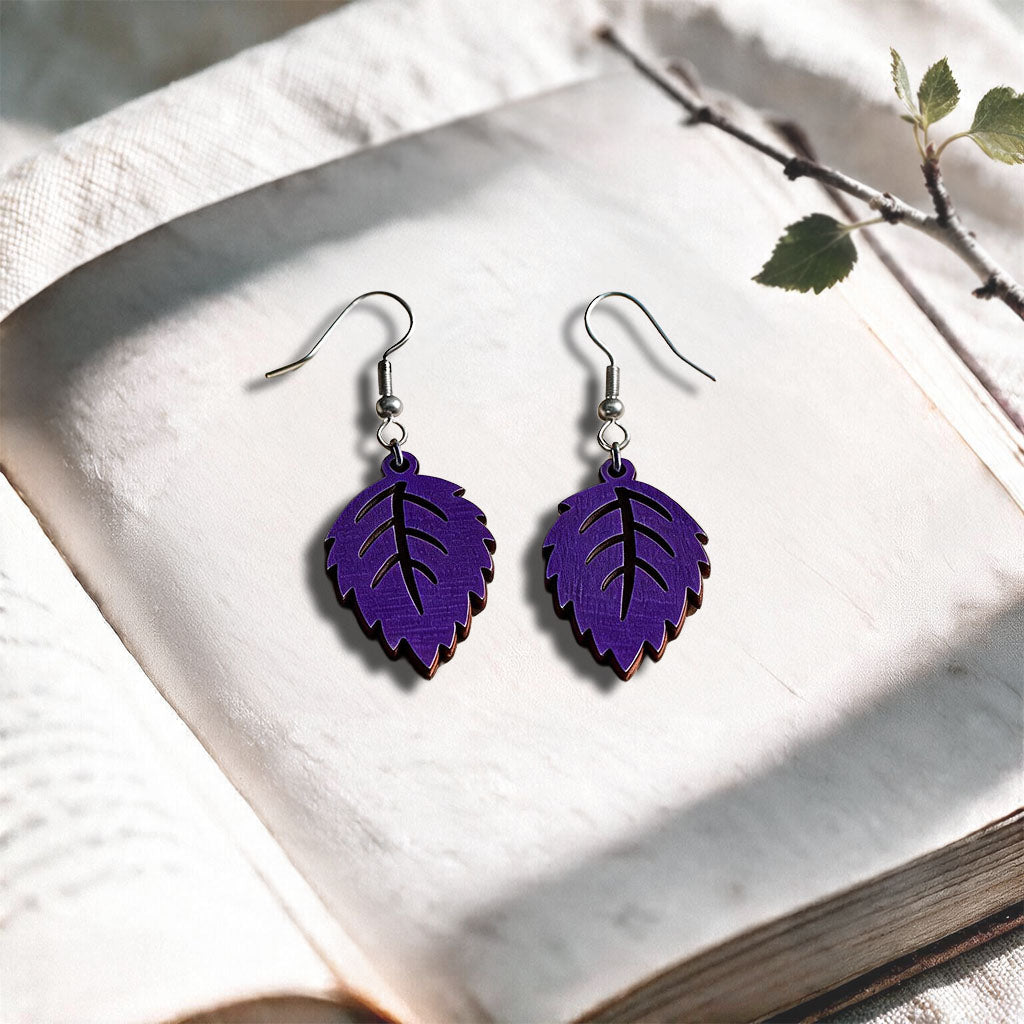 Plum Mini Birch plywood earrings made in Finland, photographed on a vintage book in natural sunlight