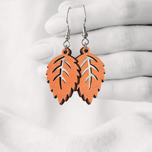 Papaya Mini Koivu (birch leaf) plywood earrings made in Finland, photographed hanging from a hand against a softly blurred light linen background.