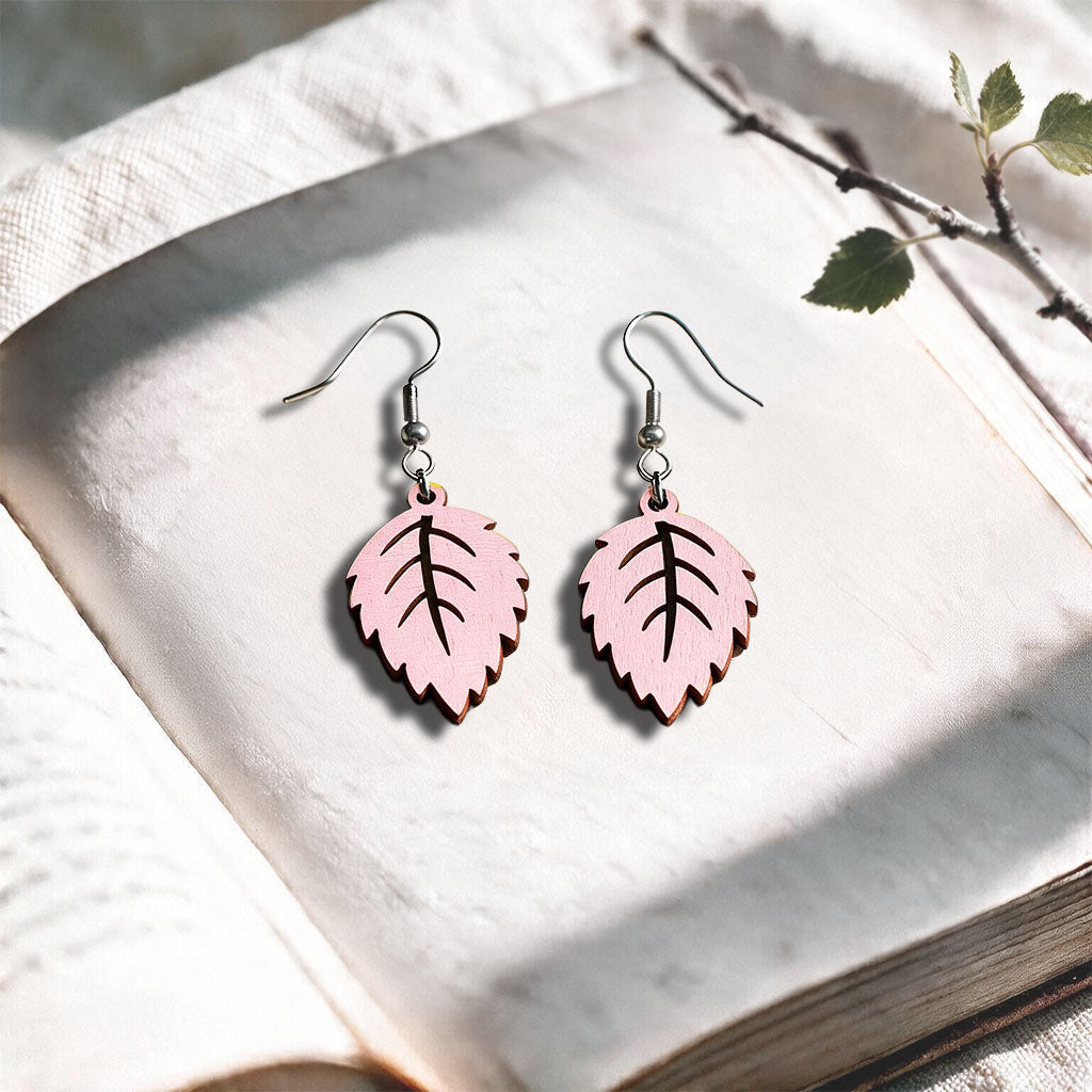 Light Pink Mini Birch plywood earrings made in Finland, photographed on a vintage book in natural sunlight