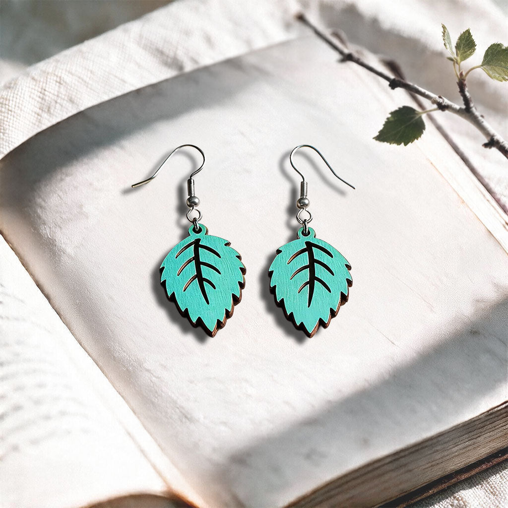 Turquoise Mini Birch plywood earrings made in Finland, photographed on a vintage book in natural sunlight