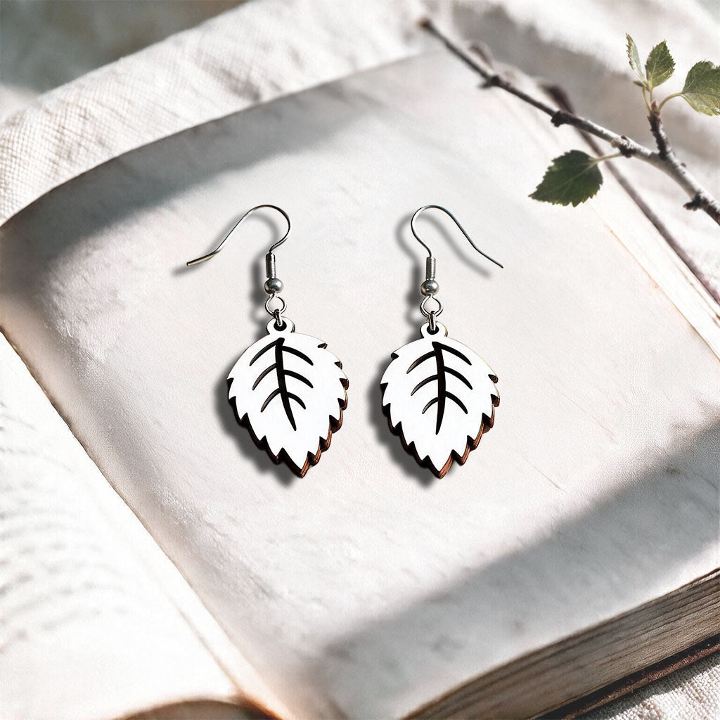 White Mini Birch plywood earrings made in Finland, photographed on a vintage book in natural sunlight